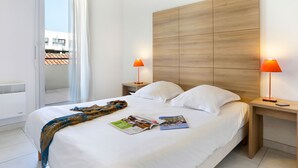 A hotel room with a large bed, two bedside tables, a wooden headboard, and a window with curtains. - Cap Med by Interhome (Le Grau du Roi)
