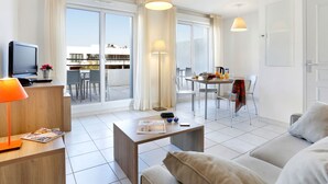 A modern living room with a sofa, coffee table, and TV. There is a balcony with a dining table and chairs. - Cap Med by Interhome (Le Grau du Roi)
