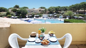 A dining table with breakfast items, a pool, and a view of a resort area. - Résidence Odalys Référence Saint Loup by Interhome (Cap d'Agde)