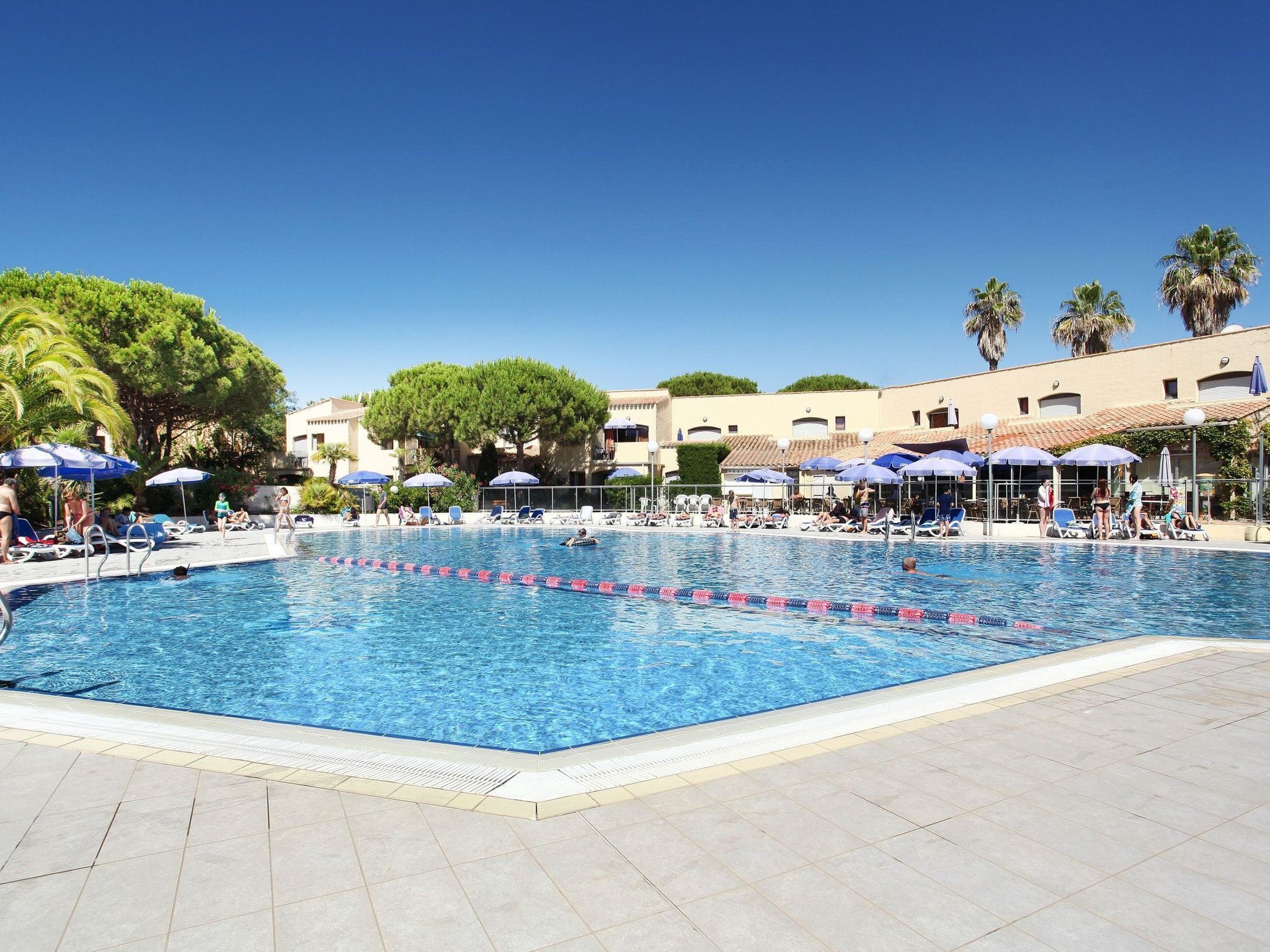 A swimming pool with lounge chairs and umbrellas, surrounded by buildings and trees.
