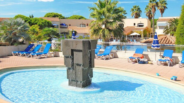 Zona de piscina con sillas reclinables azules y una fuente central.