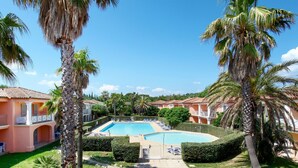 A pool area with a fountain, surrounded by palm trees and a building with a tiled roof. - Résidence Odalys Référence La Palmeraie by Interhome (Grimaud)