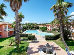 Zona de piscina con una fuente, rodeada de palmeras y un edificio con tejado de azulejos.