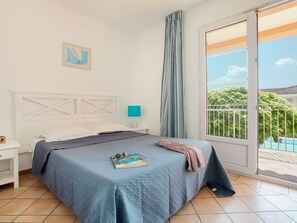 Un dormitorio con cama, mesita de noche, ventana con vista a la vegetación y un cuadro en la pared.