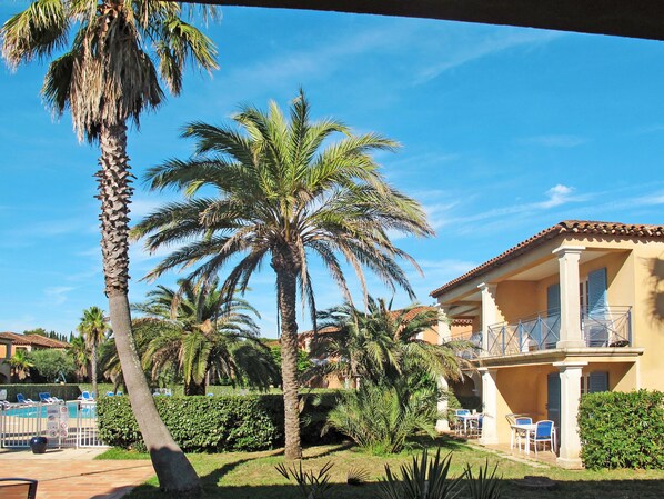 A sunny courtyard with palm trees, a pool, and a building with a balcony.