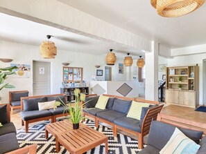 Un vaste espace de vie comprenant un ensemble de canapés, une table basse en bois et des lampes suspendues en osier.