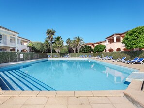 Une piscine à l’eau bleue, entourée de chaises longues et de palmiers.