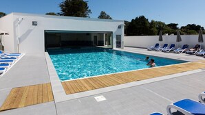 A swimming pool area with a wooden deck, lounge chairs, and a covered entrance.