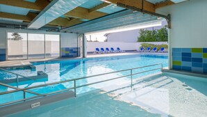 Une piscine intérieure à l’eau claire, un mur recouvert de carreaux bleus et verts, et un espace abrité avec des chaises longues bleues.