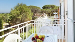 A balcony with a table set for dining, surrounded by white railings, overlooking a lush landscape with trees and a distant view of the sea. - Odalys Référence Domaine des Eucalyptus by Interhome (Saint Aygulf)