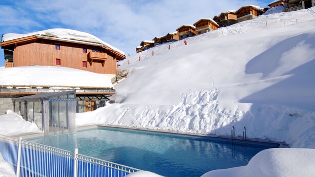 Une piscine entourée de neige, des bâtiments en bois et une piste de ski.