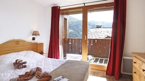 Une chambre à coucher avec un lit, un ours en peluche, un livre et une vue sur un balcon avec des rideaux rouges.