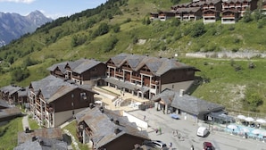 Un hôtel de style chalet traditionnel, composé de plusieurs bâtiments en bois, avec une cour centrale et un décor de montagnes en toile de fond.