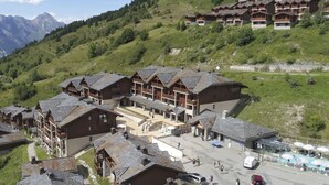 Een traditioneel hotel in chaletstijl met meerdere houten gebouwen, een centrale binnenplaats en een berg op de achtergrond.