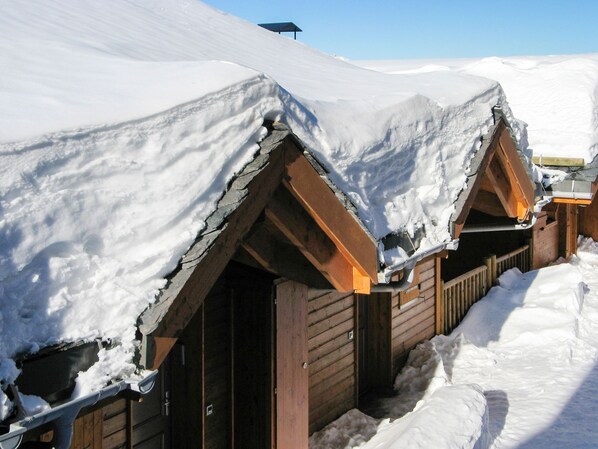 A row of wooden cabins covered in snow, with a clear sky above.