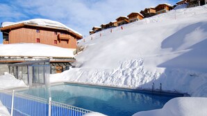 A pool surrounded by snow, wooden buildings, and a ski slope. - Odalys Référence Le Grand Panorama 1 by Interhome (Valmeinier)