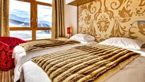 Camera d'albergo con due letti, una grande finestra vista montagne e una testiera a motivi decorativi.