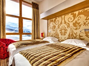 Habitación de hotel con dos camas, un ventanal con vistas a montañas y un cabecero estampado.