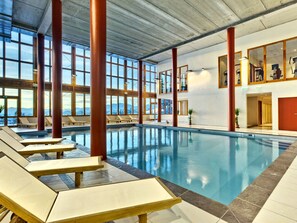 Una piscina interior con sillones de descanso, ventanas amplias y vistas a montañas.
