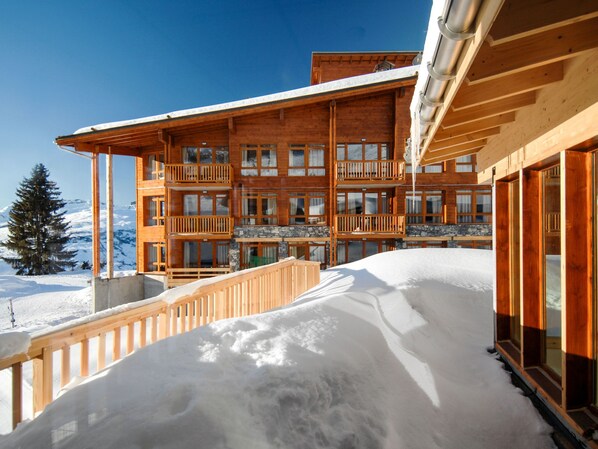 A multi-story wooden building with balconies, a stone foundation, and a snowy landscape.