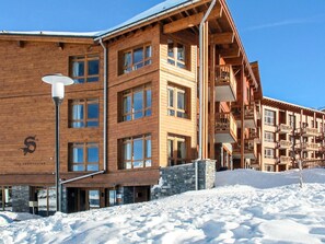 Un edificio de madera de varios pisos con ventanas y balcones amplios, rodeado de nieve.