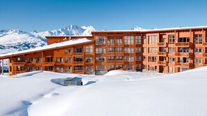 Un immeuble en bois à plusieurs étages, doté de balcons, entouré de montagnes enneigées.