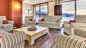 Un salon moderne avec des canapés à rayures et une table basse en bois, de grandes fenêtres offrant une vue sur les montagnes et un lampadaire.