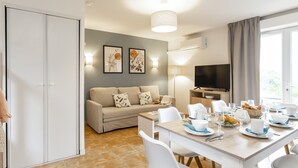 A modern hotel room with a dining area, a sofa, and a TV.