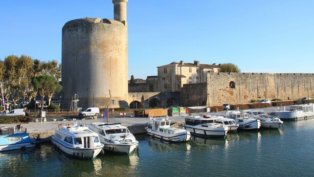 A historic tower with a minaret, surrounded by a fortified wall and a marina with several boats.
