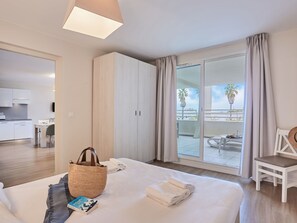 Ett hotellrum med en säng, ett sängbord, en stol, en balkong med utsikt och ett litet kök.