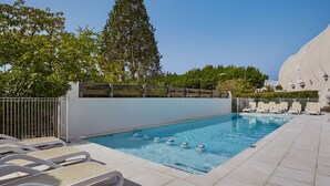 Una piscina con sillas de descanso, una valla de madera y un árbol alto al fondo.