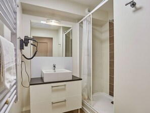 A bathroom with a white sink, a mirror, a shower with a glass door, and a towel rack.