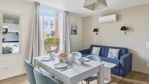 Un salon moderne avec un coin repas, un canapé bleu et une cuisine visible à travers une porte ouverte.