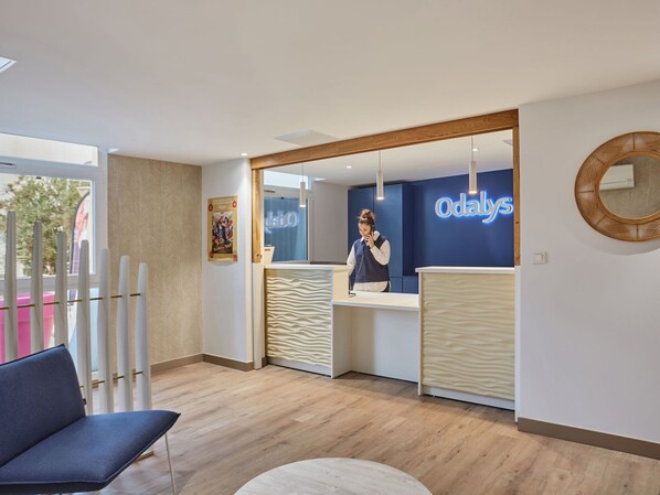 A reception area with a wooden reception desk, a blue wall with 'Odaly' signage, a mirror, and a wooden floor.