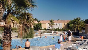 A swimming pool area with lounge chairs and palm trees. - Odalys Essentielle Le Grand Bleu by Interhome (Valras Plage)