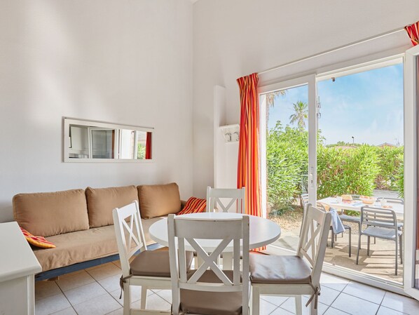 Un salón moderno con un sofá, una mesa de comedor con sillas, un ventanal con cortinas y vistas a zonas verdes.