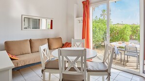 A modern living room with a sofa, two white chairs, a small table, and a sliding glass door leading to an outdoor area with a table and chairs. - Odalys Essentielle Le Grand Bleu by Interhome (Valras Plage)