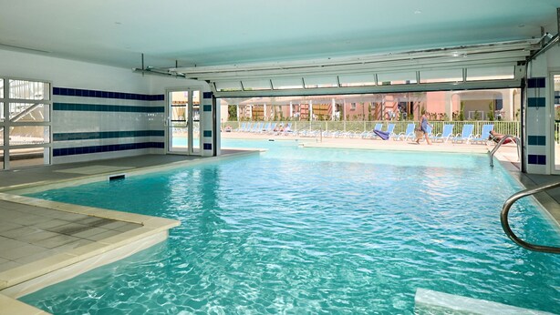 Una piscina interna con acqua cristallina, pareti piastrellate e vista su un’area con lettini.