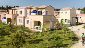 Zona residenziale con case dotate di portali ad arco e balconi, cielo sereno e un ciclista su una pista ciclabile.