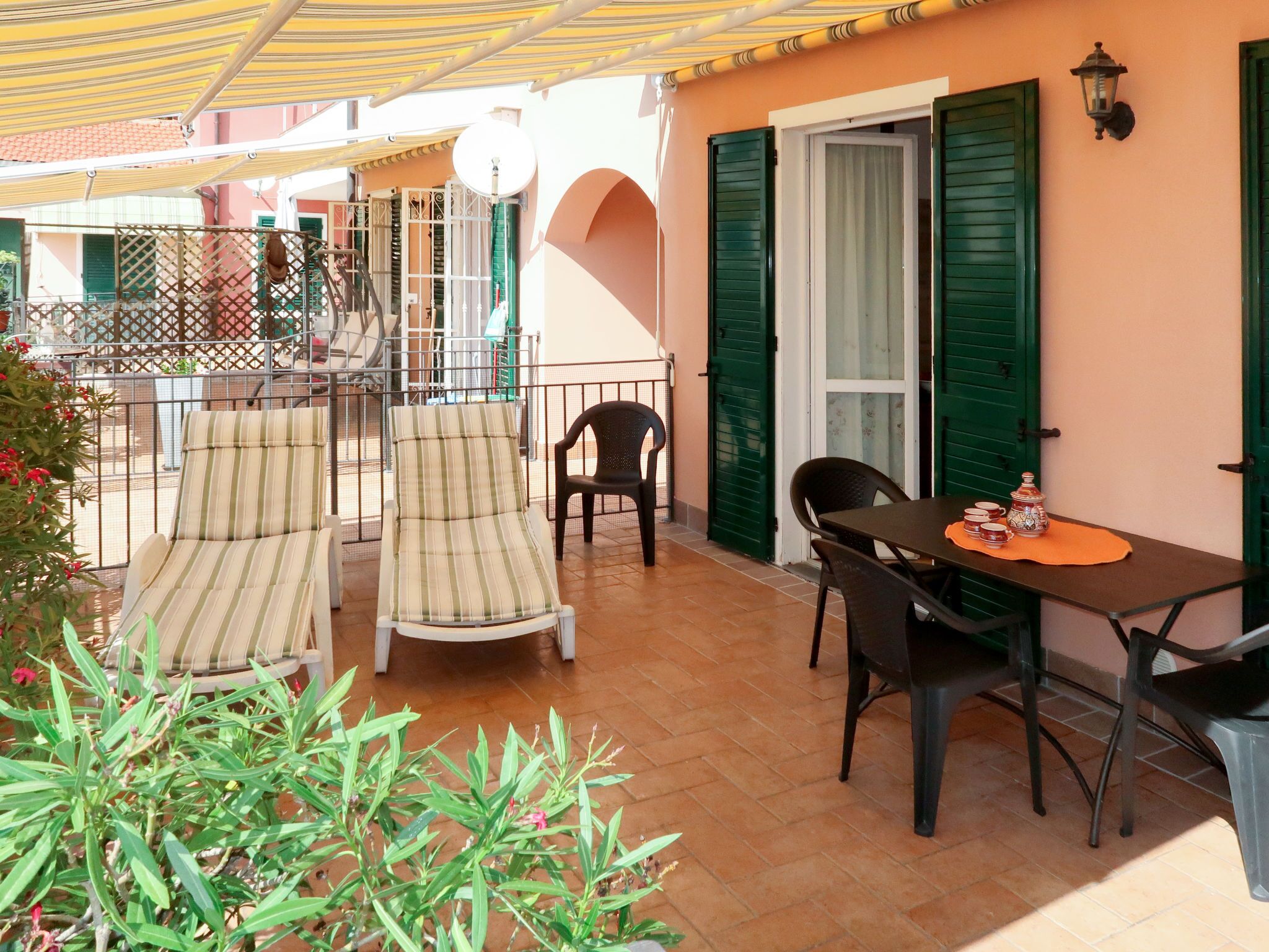 A patio with two striped chairs, a table with a vase and cups, and a green door.