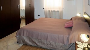 A bedroom with a bed, a nightstand with a lamp, a wardrobe, and a window with curtains. - Samuele by Interhome (Civezza)