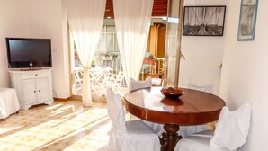 Un coin repas avec une table ronde, des chaises blanches et un téléviseur posé sur un meuble.