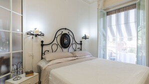 A bedroom with a bed, a bedside table, a wall-mounted clock, and a window with curtains. - Imperatrice by Interhome (Sanremo)