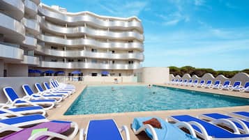 Un hotel con piscina rodeada de sillones de descanso y sombrillas.