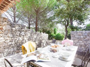 An outdoor dining area with stone walls, a table set with plates, glasses, and a basket of bread.