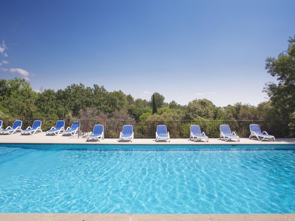 A swimming pool with clear blue water and white lounge chairs arranged along the edge.