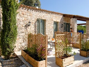 A stone building with a tiled roof, wooden lattice panels, and a garden with potted plants.