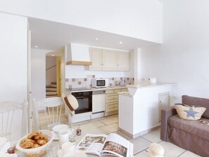 A compact kitchen with white cabinets, a microwave, and a built-in oven. There's a dining area with a table set for two, and a sofa with a star-patterned cushion.