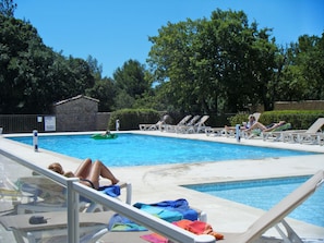 A swimming pool with lounge chairs and a person lying on one of the chairs.