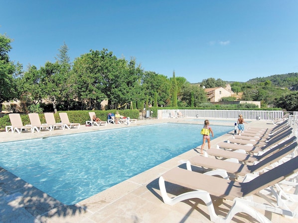 A swimming pool with lounge chairs and a person in a yellow life jacket.